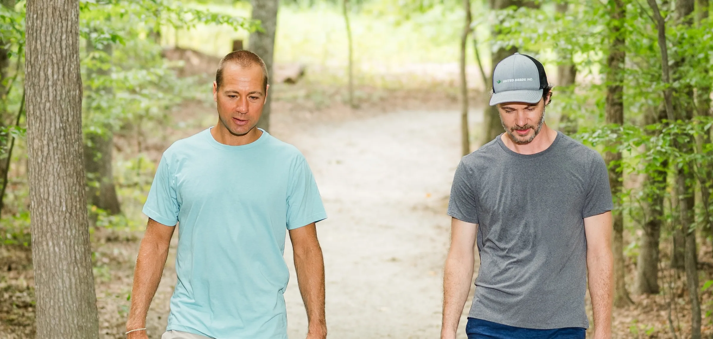 Two men walking and talking on a sunlit wooded trail at Robious Landing
